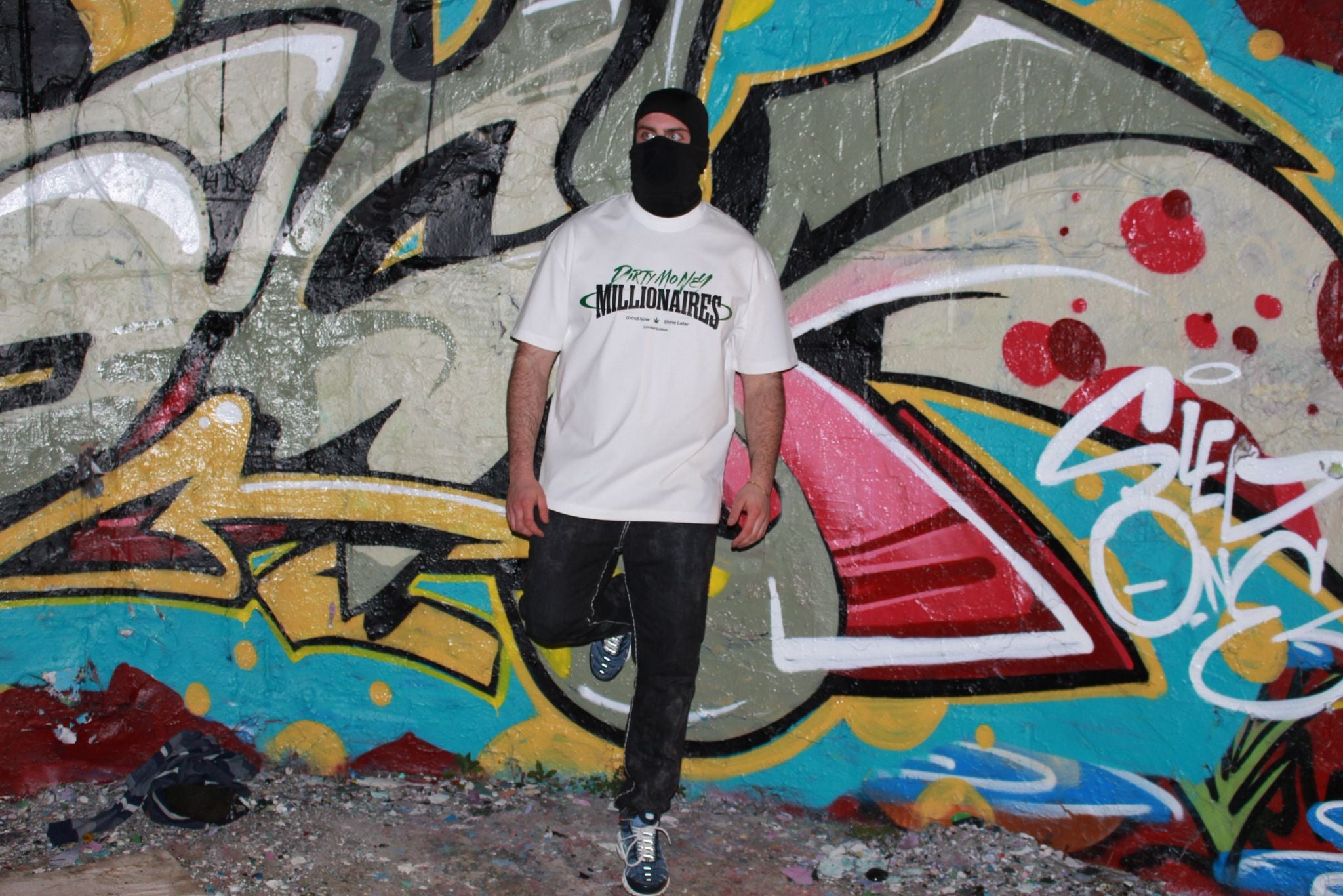 Dirty Money Millionaires model in white tee in front of graffiti wall